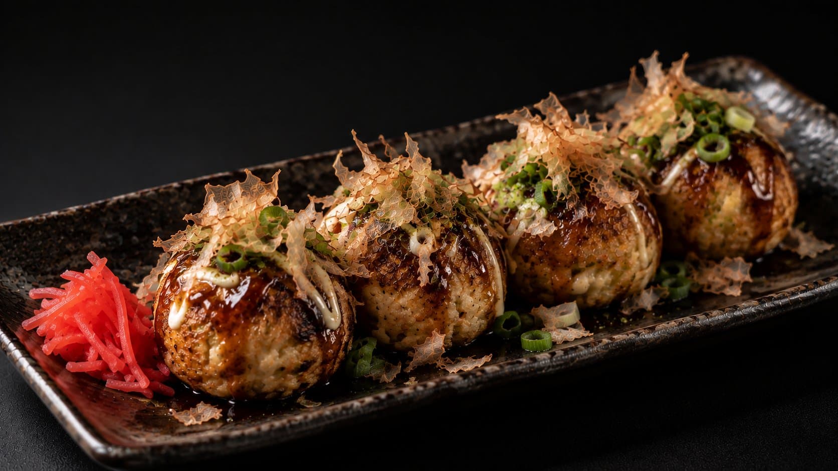 Takoyaki on a dark plate, topped with sauce, mayonnaise, bonito flakes, and green onion